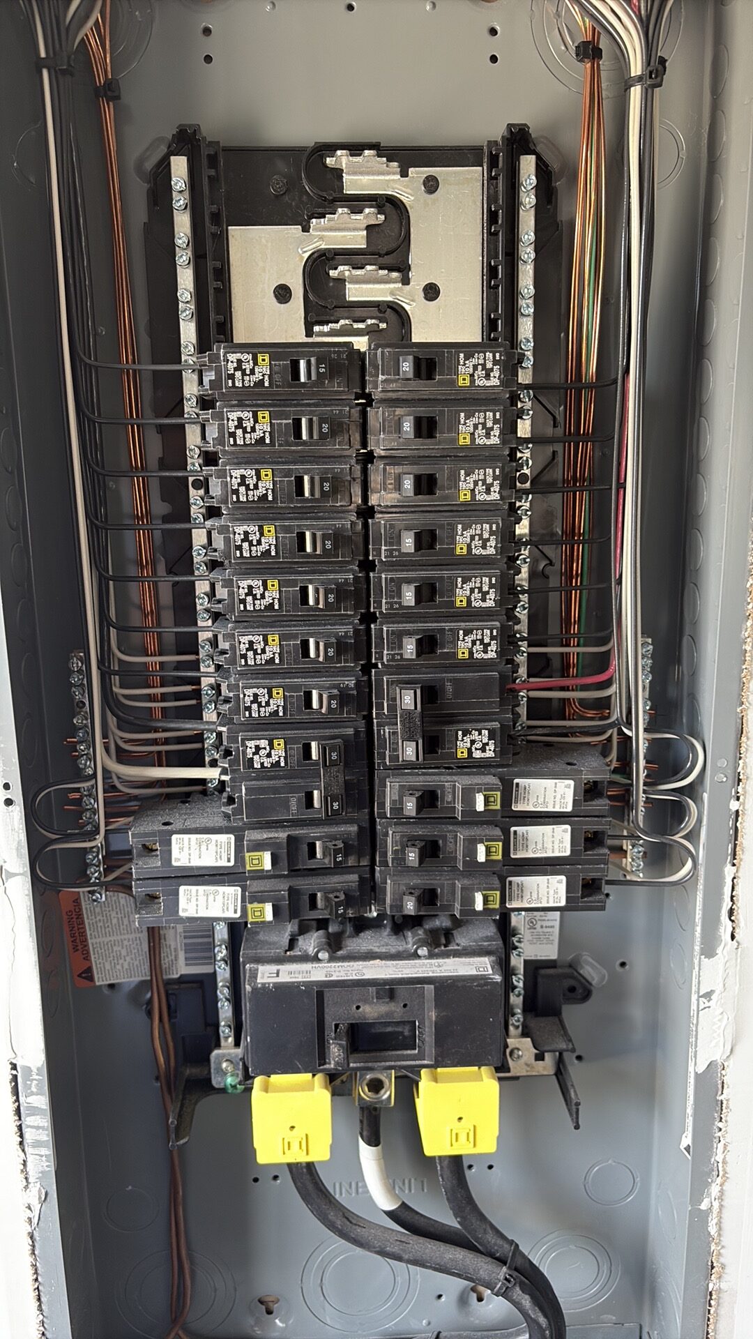 Open electrical panel with the cover removed, showing rows of circuit breakers, a main breaker at the bottom, and wiring routed along both sides.