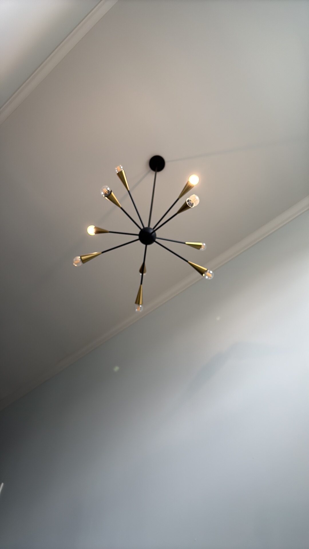A modern sputnik-style ceiling light fixture with black arms and brass tips, mounted on a sloped white ceiling.